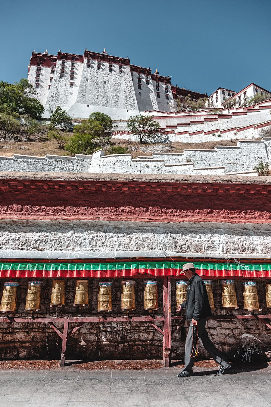 A man spins prayer wheels with the Potala Palace in the background.